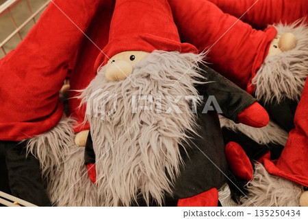 Red and gray plush gnomes with long beards displayed in a store basket. The concept represents holiday magic, coziness, and playful spirit Red and gray plush gnomes with long beards displayed in a store basket. The concept represents holiday magic, coziness, and playful spirit 135250434