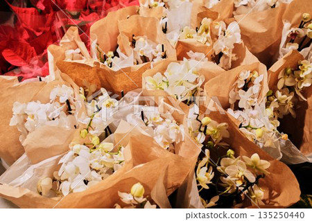 Elegant white orchids wrapped in brown paper ready for sale in a flower shop. The concept represents purity, simplicity, and refined natural beauty 135250440