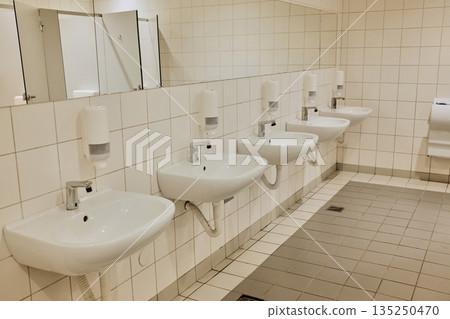 Modern restroom in mall with multiple white sinks, mirrors, and tiled walls. Concept highlights hygiene, cleanliness, and order 135250470