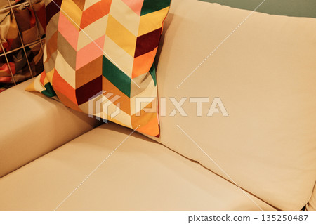 Beige sofa with a decorative pillow in colorful geometric pattern adding warmth to a cozy interior 135250487