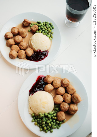 Overhead view of two identical plates of Swedish meatballs with mashed potatoes, peas, gravy, and lingonberry sauce beside glasses of soda Overhead view of two identical plates of Swedish meatballs with mashed potatoes, peas, gravy, and lingonberry sauce beside glasses of soda 135250505