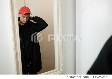 A man adjusts a red cap on his head while looking into the mirror. The moment reflects personal care and self presentation concept A man adjusts a red cap on his head while looking into the mirror. The moment reflects personal care and self presentation concept 135250550