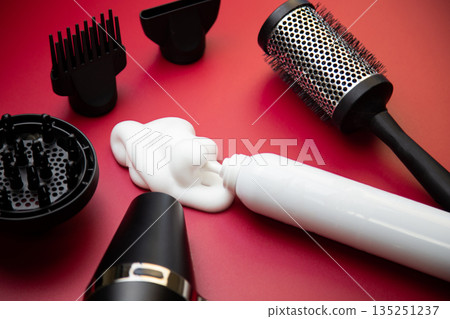 Side view of the hair styling foam in a white bottle on a pink background, surrounded by hair drying attachments, a hairdryer and a round styling comb. The concept of long-term hair styling 135251237