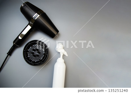 A top view of hair styling foam in a white bottle, next to it is a hairdryer with a diffuser nozzle on a gray background with space for text. The concept of long-term hair styling, creating hairstyles A top view of hair styling foam in a white bottle, next to it is a hairdryer with a diffuser nozzle on a gray background with space for text. The concept of long-term hair styling, creating hairstyles 135251240