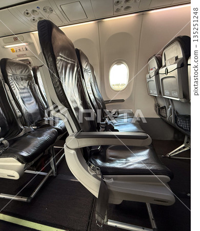 Airplane interior with black leather seats arranged near exit row and window section. Travel, mobility, and modern aviation comfort highlighting passenger transport and tourism lifestyle. 135251248
