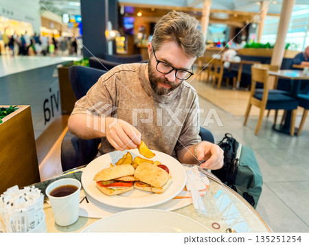 Man adding ketchup to sandwich with potato wedges in cafe. Personality, lifestyle, and dining moments in hospitality environment. Man adding ketchup to sandwich with potato wedges in cafe. Personality, lifestyle, and dining moments in hospitality environment. 135251254