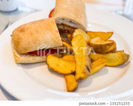 Sandwich with potato wedges served on white plate. Nutrition, refreshment, and lifestyle moments in restaurant and cafe dining. Sandwich with potato wedges served on white plate. Nutrition, refreshment, and lifestyle moments in restaurant and cafe dining. 135251255