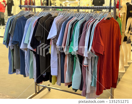 Colorful t-shorts hanging on a rack in a fashion store. Clothing variety, retail shopping, seasonal apparel, textile display and wardrobe selection. Colorful t-shorts hanging on a rack in a fashion store. Clothing variety, retail shopping, seasonal apparel, textile display and wardrobe selection. 135251271