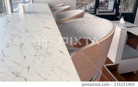 Minimalist cafe counter with marble surface and modern chairs close-up. Urban lifestyle, morning coffee culture and cozy cafe atmosphere. Minimalist cafe counter with marble surface and modern chairs close-up. Urban lifestyle, morning coffee culture and cozy cafe atmosphere. 135251405