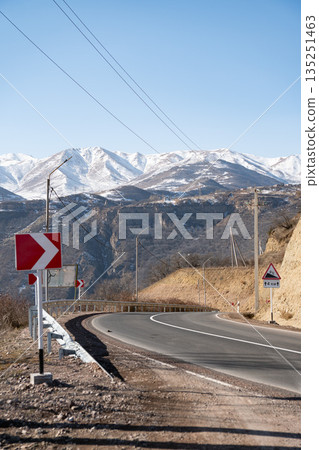 Winding mountain road curves through rocky landscape in Armenia with snow-covered peaks, blue sky, strong sense of direction and journey Winding mountain road curves through rocky landscape in Armenia with snow-covered peaks, blue sky, strong sense of direction and journey 135251463