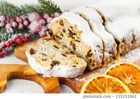 Traditional sliced Christmas stollen loaf with raisins and powdered sugar on wooden cutting board 135251661