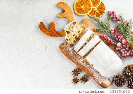 Traditional sliced Christmas stollen loaf with raisins and powdered sugar on wooden cutting board 135251663