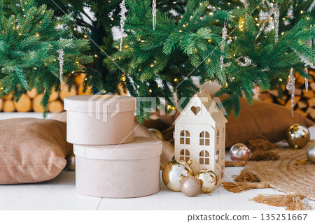 Cozy Christmas decor with round white gift boxes and decorative house under festive fir tree Cozy Christmas decor with round white gift boxes and decorative house under festive fir tree 135251667