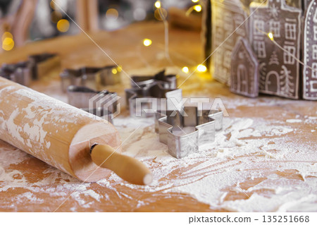 Baking gingerbread cookie cutters, wooden rolling pin, and flour are messily spread on kitchen table Baking gingerbread cookie cutters, wooden rolling pin, and flour are messily spread on kitchen table 135251668
