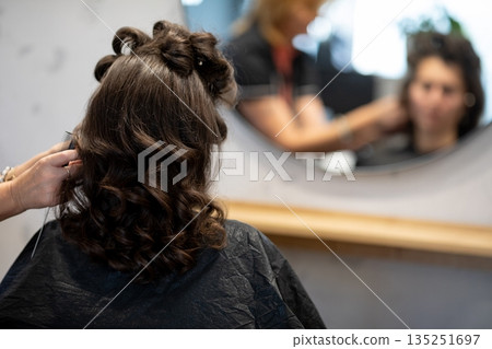 Stylist adding finishing touches to curled hair, last checks in mirror, subtle smoothing and shaping, anticipation of final look, organized station in background 135251697
