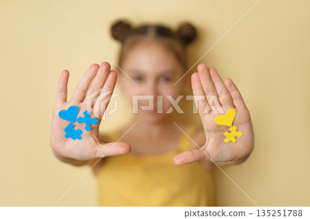 The girl shows yellow and blue puzzle pieces and hearts pasted on her palm. The concept of support, mercy and solidarity on Down Syndrome Awareness Day 135251788