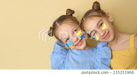 Positive children with pieces of yellow and blue puzzles and hearts on cheeks. A symbol in support of people with down syndrome. Positive children with pieces of yellow and blue puzzles and hearts on cheeks. A symbol in support of people with down syndrome. 135251908