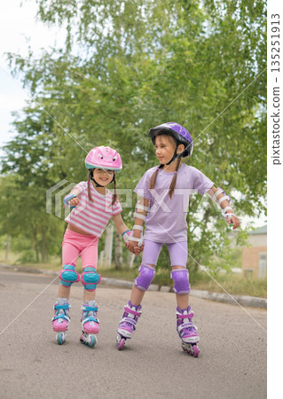 A girl teaches her younger sister how to rollerblade. Summer vacation sports A girl teaches her younger sister how to rollerblade. Summer vacation sports 135251913