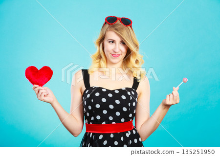 Woman holds red heart love symbol and lollipop candy Woman holds red heart love symbol and lollipop candy 135251950