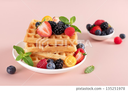 Crispy waffles with fresh berries and mint on a pink background. Breakfast or dessert menu concept Crispy waffles with fresh berries and mint on a pink background. Breakfast or dessert menu concept 135251978
