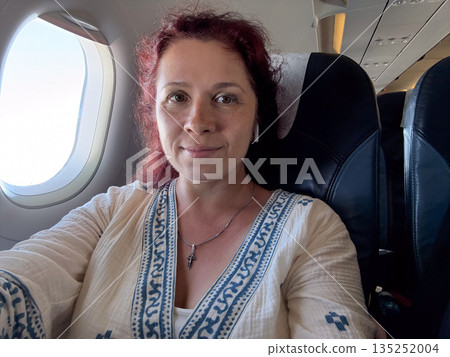 Passenger woman looking through airplane window during flight. Travel, contemplation, and personal experience of air journey. 135252004