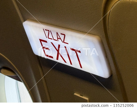 Airplane exit sign with bilingual marking. Safety, navigation, and emergency direction inside passenger aircraft. Airplane exit sign with bilingual marking. Safety, navigation, and emergency direction inside passenger aircraft. 135252006