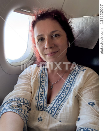 Passenger woman looking through airplane window during flight. Travel, contemplation, and personal experience of air journey. 135252007
