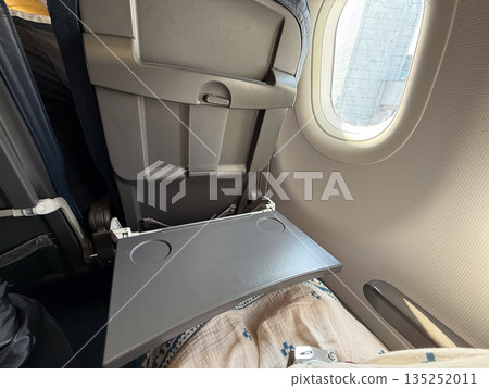 Airplane passenger opening tray table on the seat. Comfort, convenience, and in-flight functionality during travel. 135252011