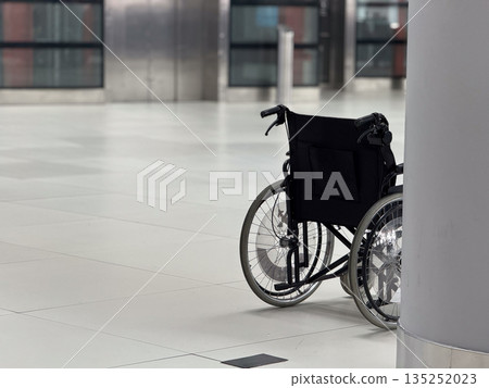 Close view of empty wheelchair positioned beside airport column copy space. Mobility assistance concept, accessibility services, inclusive travel environment, and support infrastructure in public Close view of empty wheelchair positioned beside airport column copy space. Mobility assistance concept, accessibility services, inclusive travel environment, and support infrastructure in public 135252023