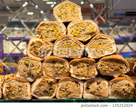 Pistachio filled nougat rolls coated in green crumbs stacked in a pyramid display in Istanbul bazaar. Luxury sweetness, artisanal skill, indulgent texture, and premium confectionery craftsmanship 135252024