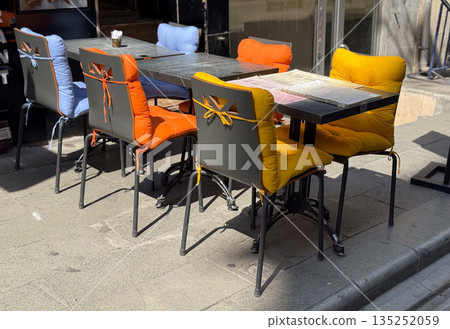 Outdoor cafe with chairs and tables, and bright yellow and red pillows. Hospitality, comfort, and lifestyle in an urban social setting. Outdoor cafe with chairs and tables, and bright yellow and red pillows. Hospitality, comfort, and lifestyle in an urban social setting. 135252059