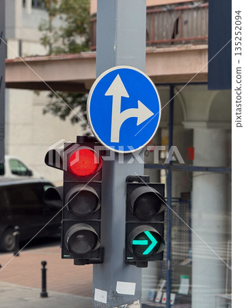 Traffic light with red stop signal and green right arrow near road sign on urban street. Transportation control, safety, regulation, direction, infrastructure, order, urban mobility and city 135252094