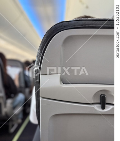 Aircraft cabin interior with passenger seat back and safety instructions. Aviation, travel, and passenger service equipment for flight safety and onboard comfort system. 135252103