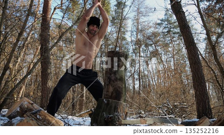 Shirtless young man chopping firewood in a sunny winter forest. Muscular guy working with axe in snowy woodland. Concept of strength, masculine, energy and harmony with nature during cold season Shirtless young man chopping firewood in a sunny winter forest. Muscular guy working with axe in snowy woodland. Concept of strength, masculine, energy and harmony with nature during cold season 135252216