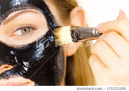 Woman applying black mud mask to face 135252260