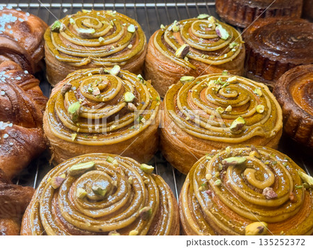 Pistachio spiral buns arranged on a pastry rack behind glass. Bakery craftsmanship, nut glaze, and premium dessert presentation Pistachio spiral buns arranged on a pastry rack behind glass. Bakery craftsmanship, nut glaze, and premium dessert presentation 135252372
