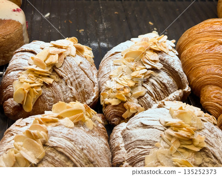 Almond croissants dusted with sugar on a bakery tray. Artisan pastry, nut topping, and breakfast indulgence in a patisserie display Almond croissants dusted with sugar on a bakery tray. Artisan pastry, nut topping, and breakfast indulgence in a patisserie display 135252373