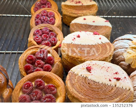 Raspberry filled laminated pastries and iced rounds in a bakery showcase. Fruit dessert appeal, patisserie craft, and premium sweet presentation 135252376
