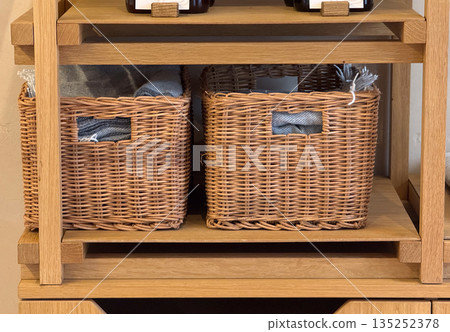 Wicker storage baskets on wooden shelving with folded fabric inside. Home organization, interior storage, and natural material decor for modern living 135252378