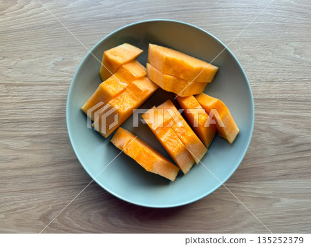 Fresh sliced cantaloupe arranged on a ceramic plate on a wooden table top view. Healthy nutrition, summer refreshment, and minimal food styling in natural light 135252379