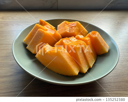 Fresh sliced cantaloupe arranged on a ceramic plate on a wooden table. Healthy nutrition, summer refreshment, and minimal food styling in natural light 135252380