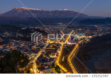 Night cityscape with modern residential buildings, illuminated streets, dense urban center and snow mpuntains peaks, Berat, Albania Night cityscape with modern residential buildings, illuminated streets, dense urban center and snow mpuntains peaks, Berat, Albania 135252397