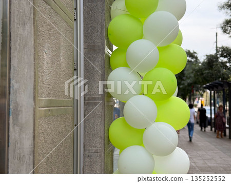 Green and white balloons decorating a shop entrance on a city street. Retail promotion, festive atmosphere, and event marketing display Green and white balloons decorating a shop entrance on a city street. Retail promotion, festive atmosphere, and event marketing display 135252552