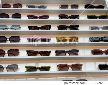 Wall display of colorful sunglasses in modern optical store. Fashion, consumer choice, lifestyle, and visual merchandising through eyewear collection 135252656