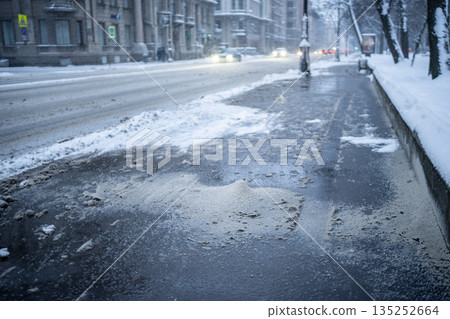 Deicing chemicals on snowy street in winter. Slippery road sprinkled with technical salt 135252664
