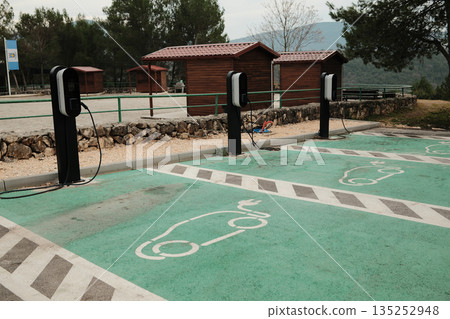 Electric vehicle charging stations in outdoor parking area near wooden buildings. Sustainable transport infrastructure with green markings and eco mobility concept 135252948