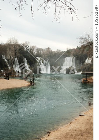 Wide cascading Kravica Waterfall surrounded by forest and turquoise river water in Bosnia and Herzegovina. Natural landscape with flowing streams, mist and calm atmosphere in early spring Wide cascading Kravica Waterfall surrounded by forest and turquoise river water in Bosnia and Herzegovina. Natural landscape with flowing streams, mist and calm atmosphere in early spring 135252997