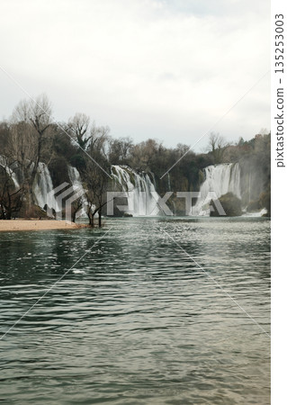 Wide cascading Kravica Waterfall surrounded by forest and turquoise river water in Bosnia and Herzegovina. Natural landscape with flowing streams, mist and calm atmosphere in early spring Wide cascading Kravica Waterfall surrounded by forest and turquoise river water in Bosnia and Herzegovina. Natural landscape with flowing streams, mist and calm atmosphere in early spring 135253003