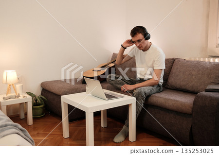 A man puts on headphones while getting ready to use his laptop. The concept highlights focus and digital work in a calm home setting 135253025