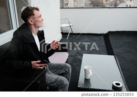 A man sits on a terrace smoking a cigarette and looking into the distance. The scene conveys a reflective morning concept A man sits on a terrace smoking a cigarette and looking into the distance. The scene conveys a reflective morning concept 135253053